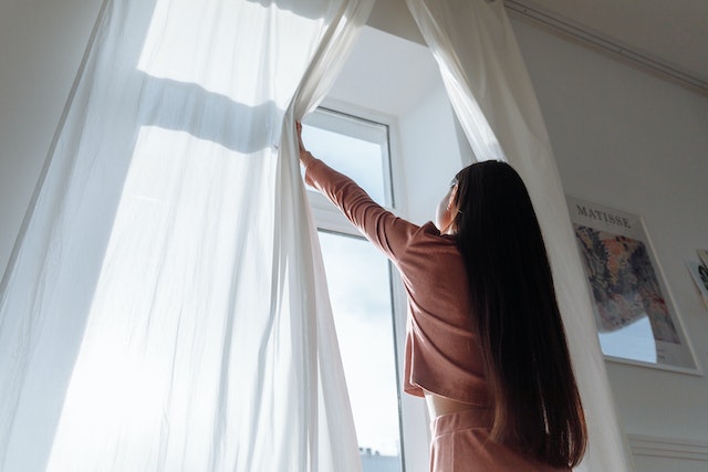 Person with long dark hair opening white curtains